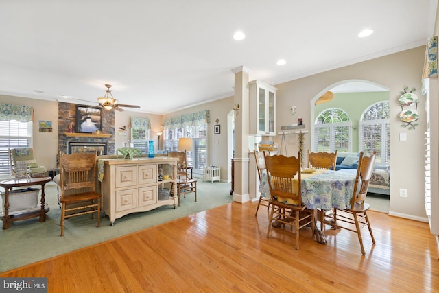 dining room with plenty of natural light, a ceiling fan, arched walkways, light wood-type flooring, and a fireplace