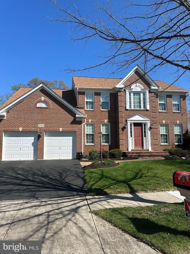 colonial-style house with brick siding, driveway, a front yard, and a garage