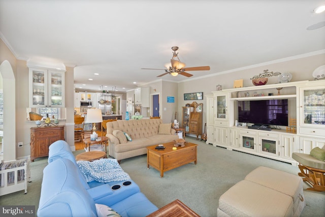 living room featuring light colored carpet, ceiling fan, arched walkways, and ornamental molding