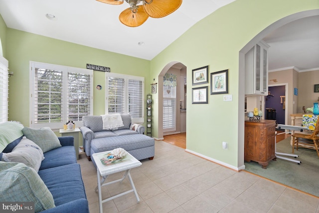 living room with arched walkways, light tile patterned flooring, vaulted ceiling, baseboards, and ceiling fan