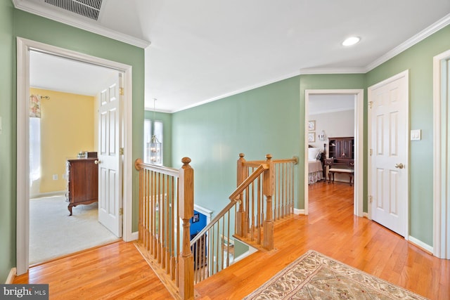 hallway with wood finished floors, ornamental molding, and an upstairs landing
