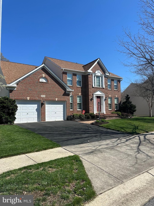 colonial house with an attached garage, brick siding, aphalt driveway, and a front yard