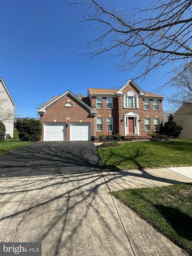 colonial-style house featuring a front lawn, brick siding, aphalt driveway, and a garage