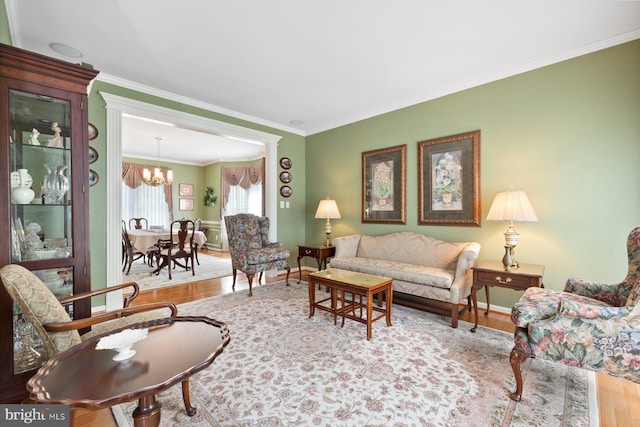 living area with baseboards, wood finished floors, a notable chandelier, and ornamental molding