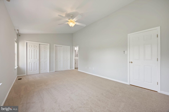 unfurnished bedroom with vaulted ceiling, multiple closets, carpet, baseboards, and visible vents