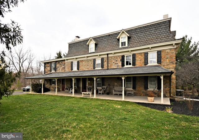 rear view of house with a yard, mansard roof, a chimney, and covered porch