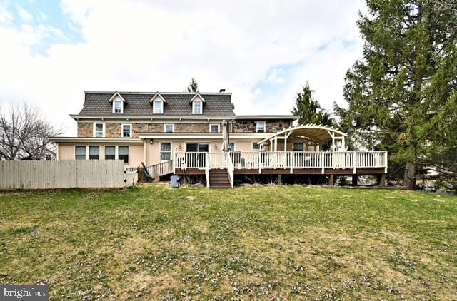 back of house featuring fence, a wooden deck, a yard, and mansard roof