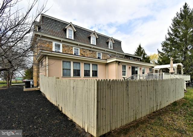 view of home's exterior with mansard roof and fence