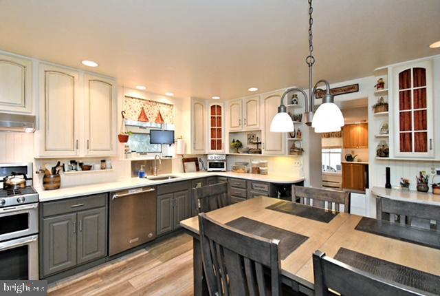 kitchen featuring recessed lighting, gray cabinetry, open shelves, under cabinet range hood, and appliances with stainless steel finishes