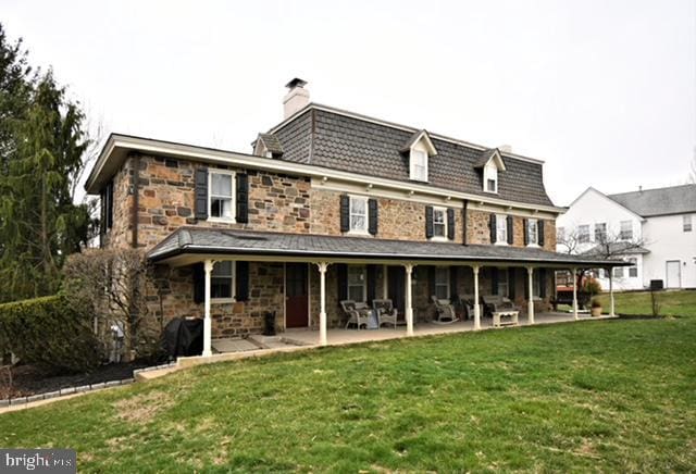 back of property with a chimney, stone siding, a yard, and a patio
