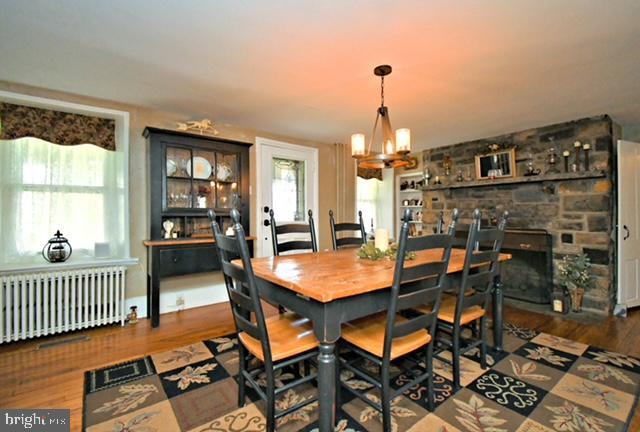 dining space featuring radiator heating unit, a stone fireplace, wood finished floors, and a notable chandelier