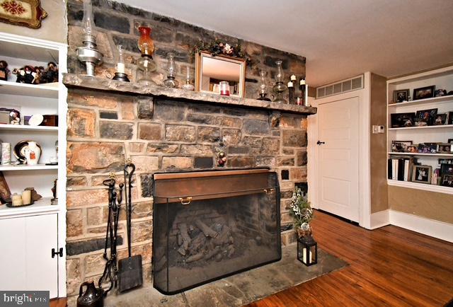 living area with wood finished floors, baseboards, a stone fireplace, and visible vents