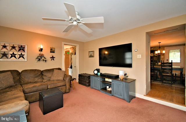 living area with baseboards, light carpet, and ceiling fan with notable chandelier
