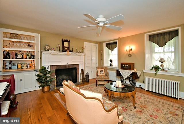 living area with radiator heating unit, hardwood / wood-style flooring, a fireplace, and a ceiling fan
