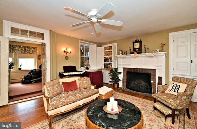 living area featuring a baseboard heating unit, ceiling fan, a brick fireplace, and wood finished floors
