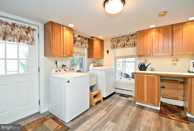 washroom with a baseboard heating unit, a healthy amount of sunlight, washer and dryer, and cabinet space