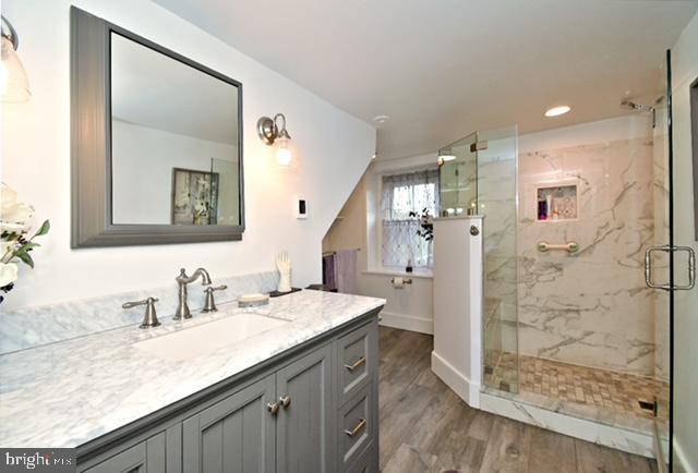 bathroom featuring wood finished floors, a marble finish shower, vanity, baseboards, and recessed lighting