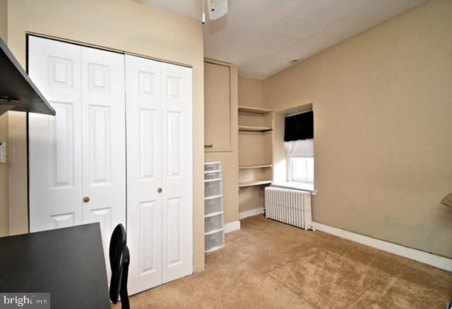 unfurnished bedroom featuring a ceiling fan, a closet, carpet floors, radiator, and baseboards