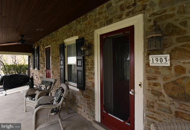doorway to property featuring stone siding, ceiling fan, and covered porch
