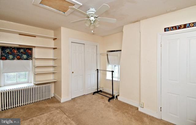 unfurnished bedroom with attic access, baseboards, carpet, radiator heating unit, and a ceiling fan