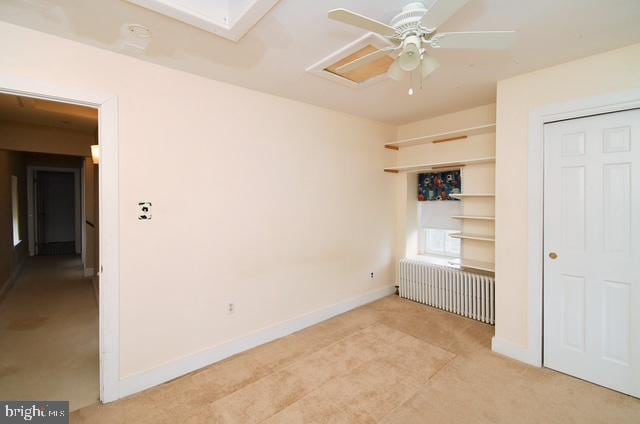 unfurnished bedroom featuring light carpet, baseboards, and radiator