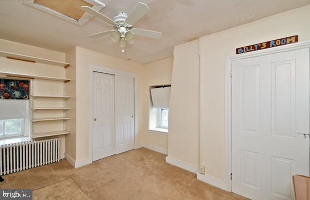 unfurnished bedroom with a ceiling fan, carpet floors, radiator heating unit, and baseboards