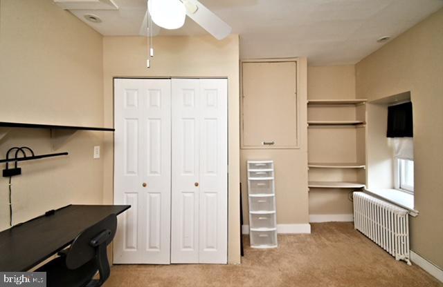 unfurnished office featuring radiator, a ceiling fan, baseboards, and light carpet
