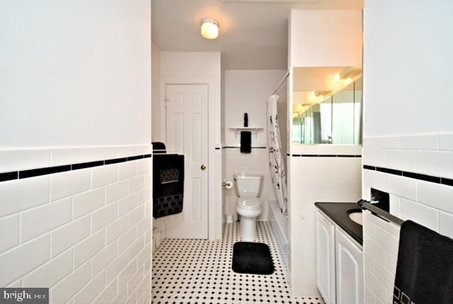 full bath featuring tile walls, toilet, and a wainscoted wall