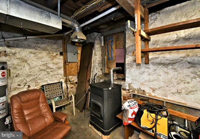 unfinished basement featuring electric panel and a wood stove