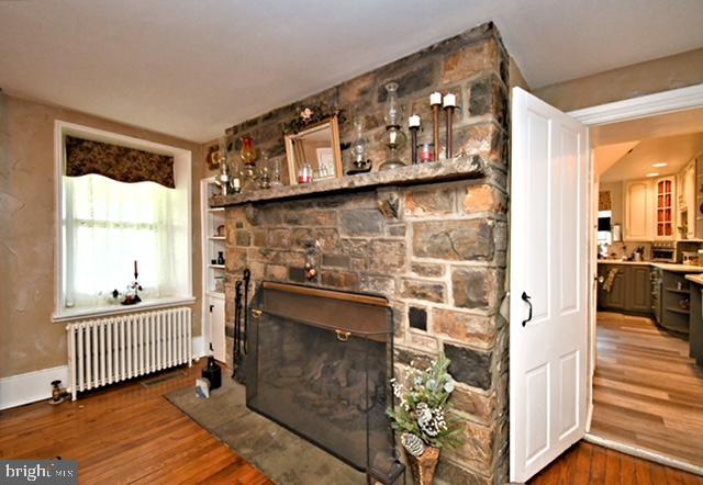 living area featuring radiator, wood finished floors, baseboards, and a stone fireplace