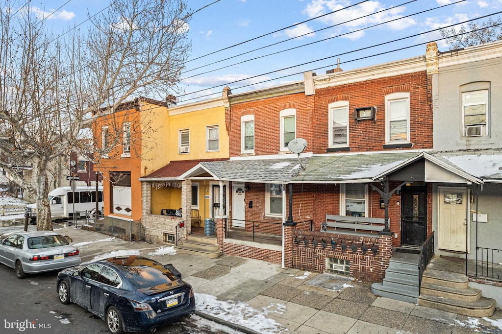 multi unit property with cooling unit, a shingled roof, covered porch, and brick siding