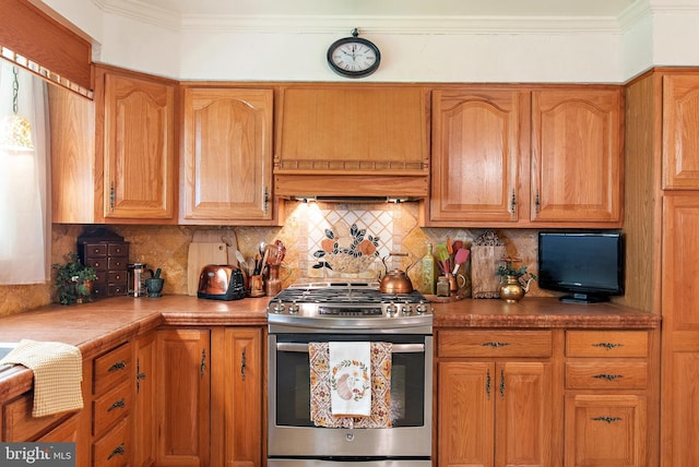 kitchen featuring stainless steel range with gas cooktop, backsplash, brown cabinetry, and custom exhaust hood