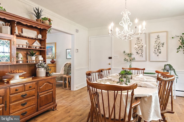dining area with crown molding, light wood-style flooring, a wainscoted wall, and a notable chandelier