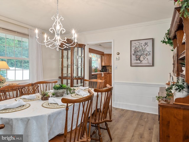 dining space with a wainscoted wall, ornamental molding, wood finished floors, and a notable chandelier
