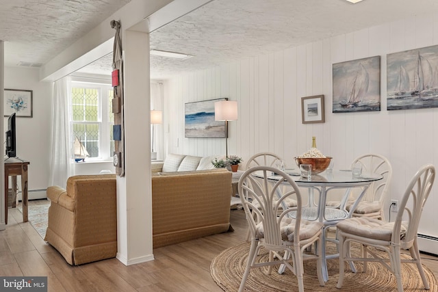 dining room with a textured ceiling, baseboard heating, wood finished floors, and visible vents
