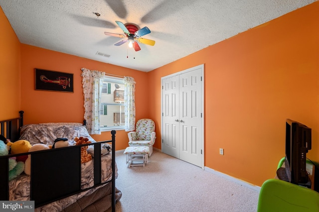 carpeted bedroom featuring visible vents, a closet, a textured ceiling, and ceiling fan