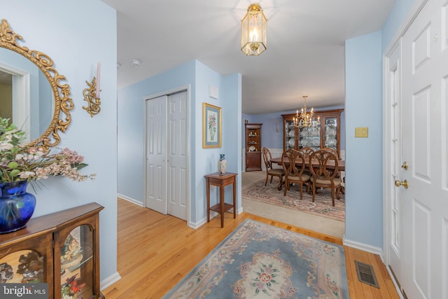 foyer featuring a notable chandelier, light wood finished floors, visible vents, and baseboards