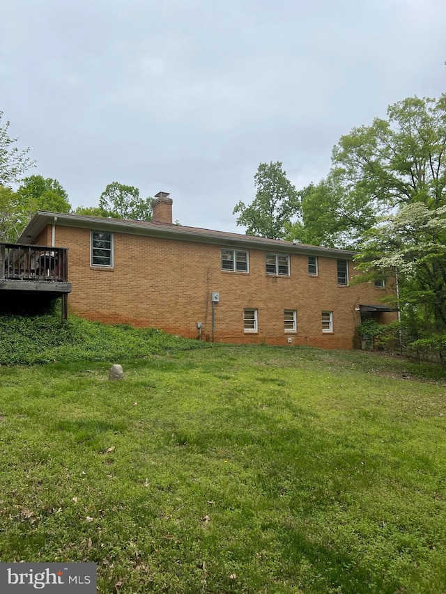 back of house featuring a chimney, brick siding, and a yard