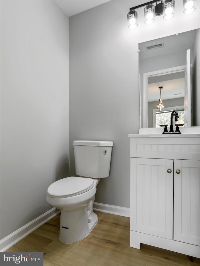 half bathroom with baseboards, wood finished floors, visible vents, and toilet