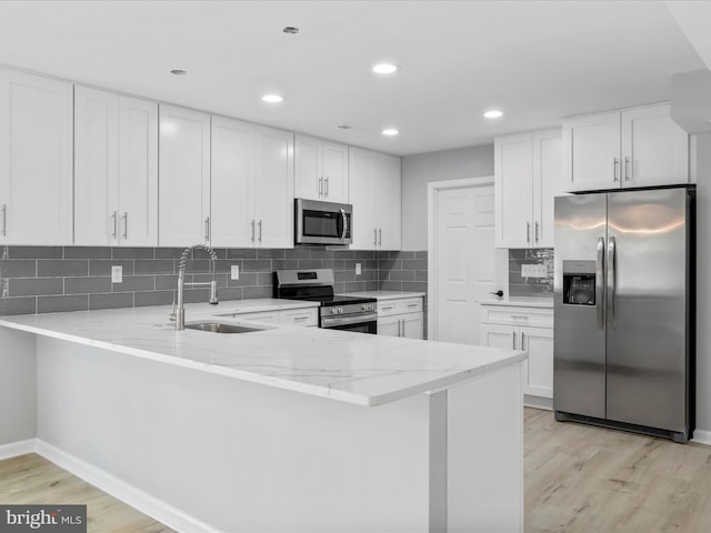 kitchen featuring stainless steel appliances, a peninsula, light wood-style flooring, a sink, and light stone counters