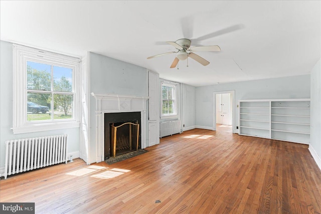 unfurnished living room with baseboards, radiator heating unit, a premium fireplace, ceiling fan, and wood-type flooring