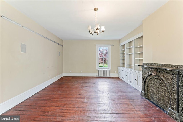 unfurnished living room featuring radiator, baseboards, built in features, a notable chandelier, and wood-type flooring