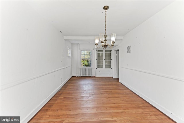 unfurnished dining area with radiator heating unit, wood finished floors, visible vents, baseboards, and a chandelier