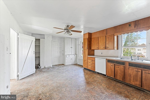 kitchen featuring white dishwasher, a sink, brown cabinets, ceiling fan, and light countertops