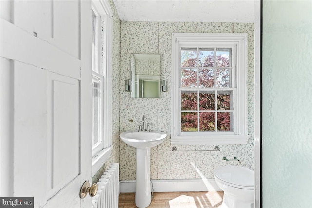 bathroom with wallpapered walls, baseboards, toilet, and radiator