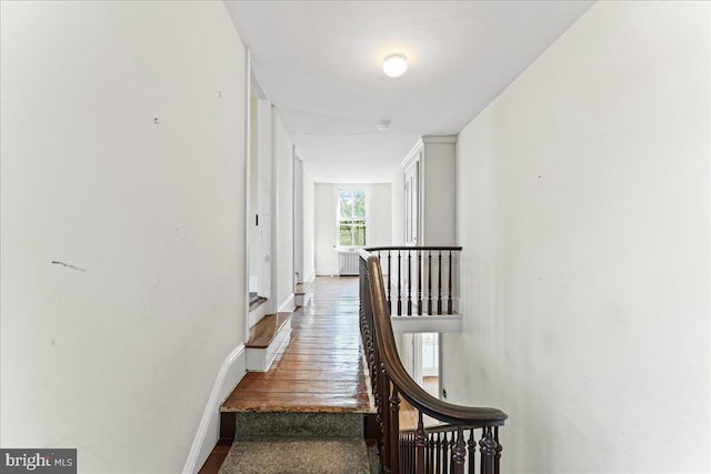 corridor featuring wood finished floors, baseboards, and an upstairs landing