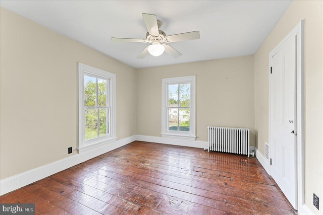 empty room featuring radiator heating unit, a wealth of natural light, baseboards, and hardwood / wood-style floors