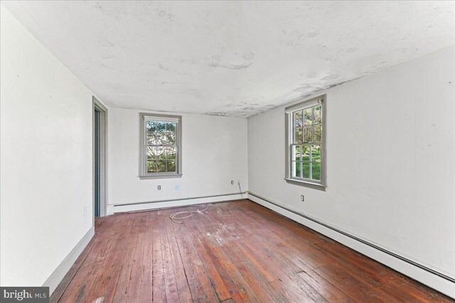 unfurnished room featuring a baseboard heating unit, wood-type flooring, and baseboards