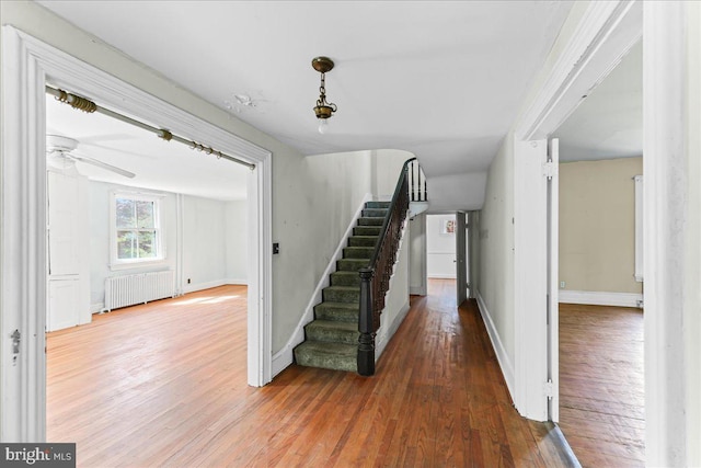 stairway with radiator, hardwood / wood-style floors, a ceiling fan, and baseboards