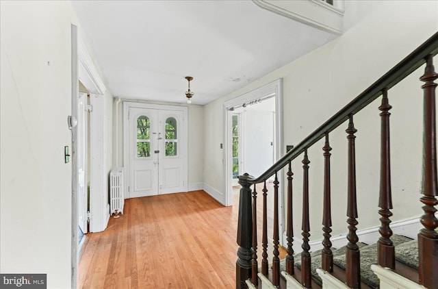foyer featuring light wood-style floors, radiator heating unit, baseboards, and stairway